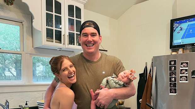 Tom and Rachael Sullivan pose in their kitchen holding their newborn baby